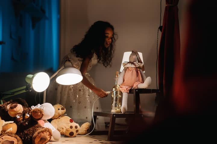 A young girl in a dress playing with toys and lamps in a softly lit room.