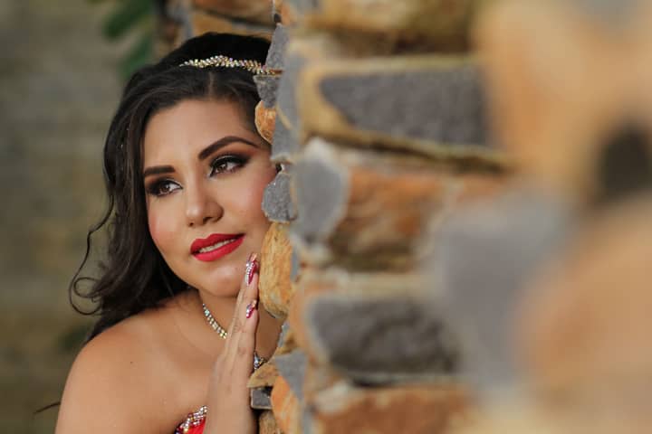 A stunning portrait of a woman with elegant makeup against a textured stone wall.