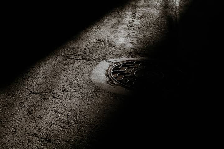 From above of manhole with metal cover on rough asphalt road at night