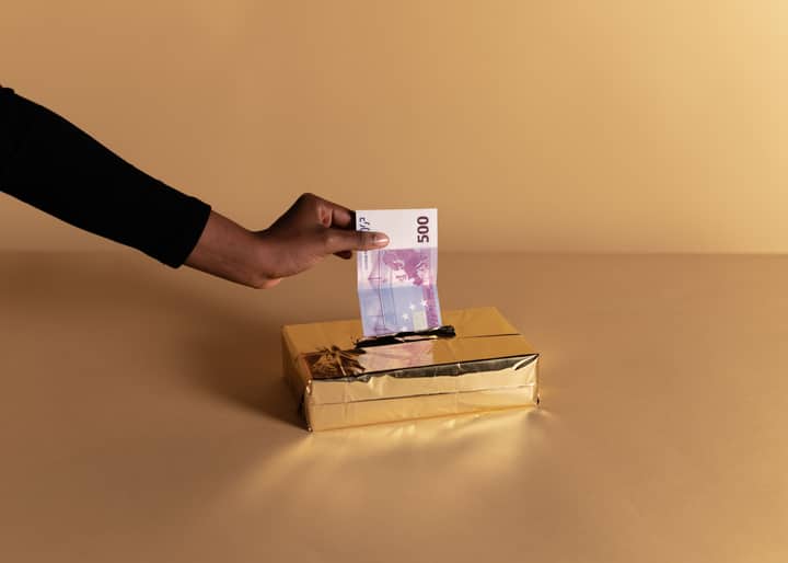 Euro banknote held by a hand against beige background, symbolizing bribery or gifting.