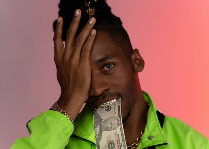 Portrait of a stylish man covering one eye with a dollar bill in a neon jacket.
