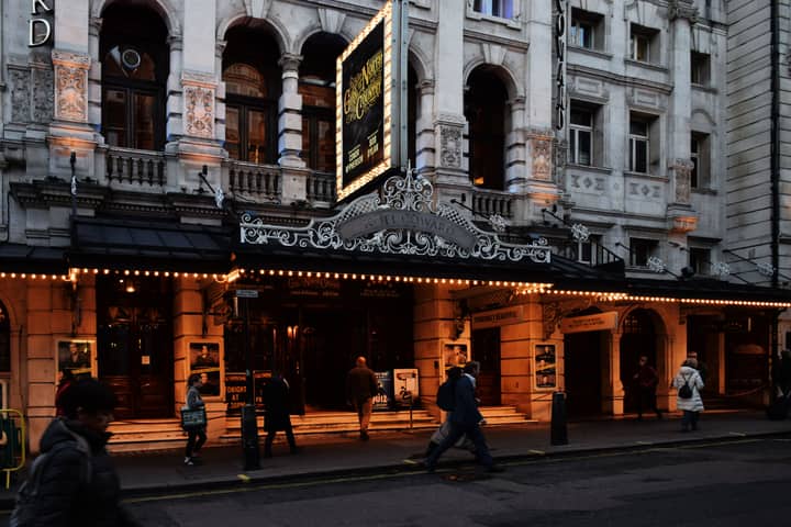 People walking by an illuminated theater in Central London at night, showcasing urban night life.