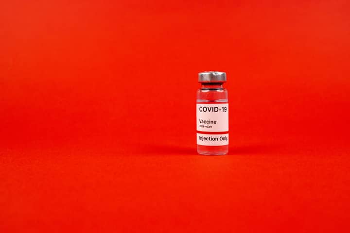 Glass vial of COVID-19 vaccine on a vibrant red backdrop, emphasizing protection.