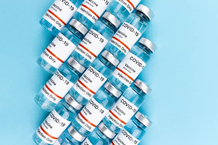 Top view of COVID-19 vaccine vials arranged on a blue surface, highlighting vaccination and pandemic themes.