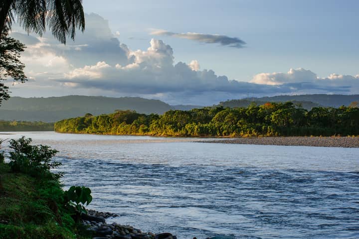 Beautiful landscape of the Tena River with lush green forest and blue sky.