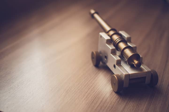 Close-up of a brass and silver miniature cannon toy placed on a wooden table.