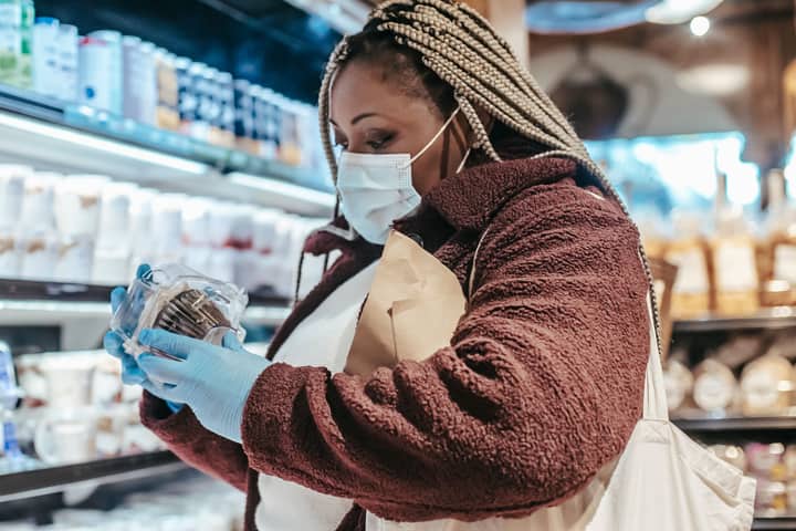 Side view of African American woman in protective gloves and mask reading sticker on product in grocery store