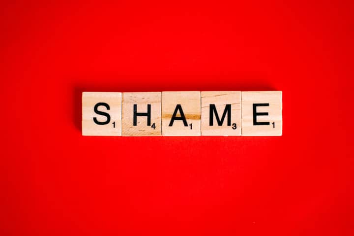 Scrabble tiles spelling the word 'Shame' on a vibrant red backdrop.