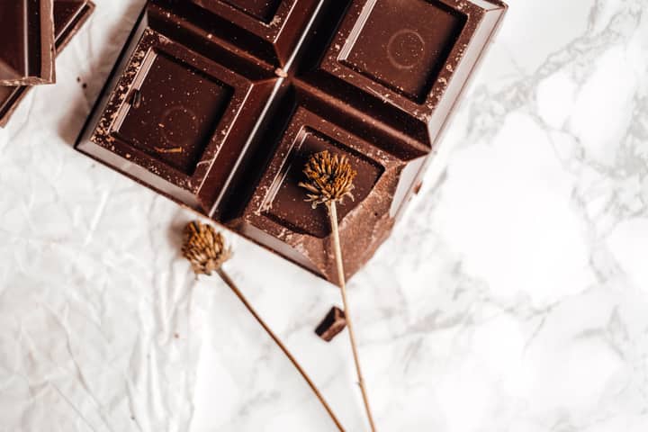 Close-up of a dark chocolate bar on marble with dried flowers, showcasing elegance in food photography.