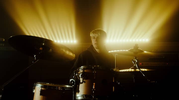 Musician passionately playing drums under warm concert lighting.