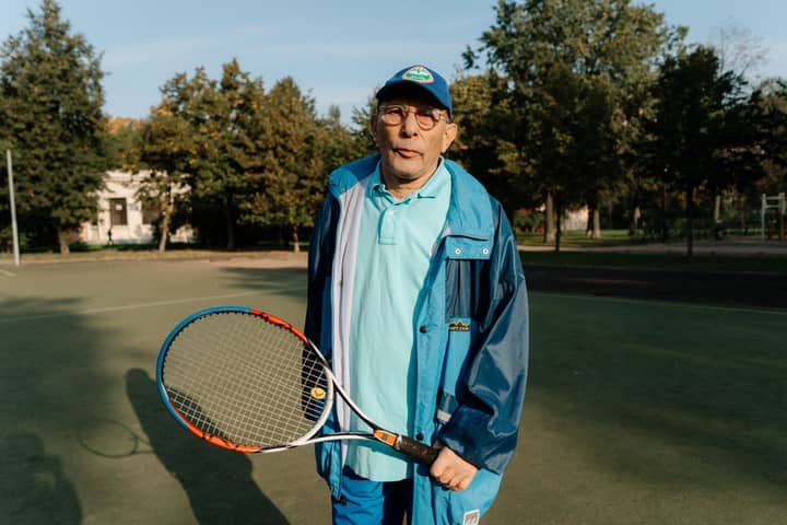 Elderly man with tennis racket on court, enjoying a sunny day of leisure and sport.