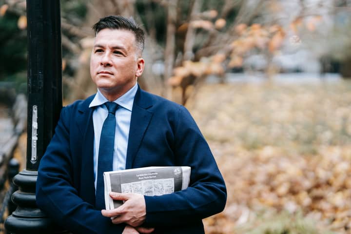 A confident businessman in formal attire stands outdoors holding a newspaper, exuding professionalism.