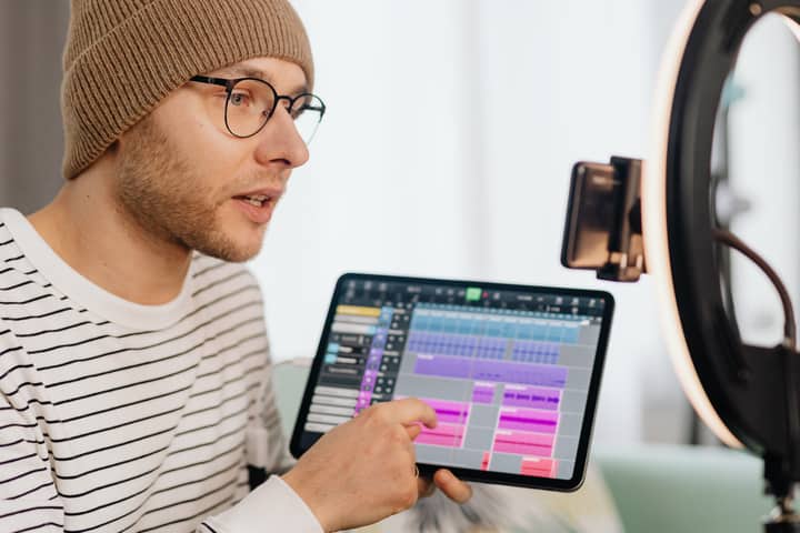 Young man composing music using a tablet and ring light indoors.