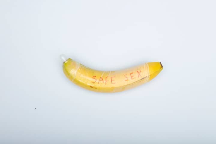 A banana wrapped with a condom symbolizing safe sex on a white background.
