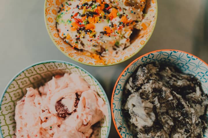 Top view of three colorful bowls filled with various ice cream flavors and toppings.