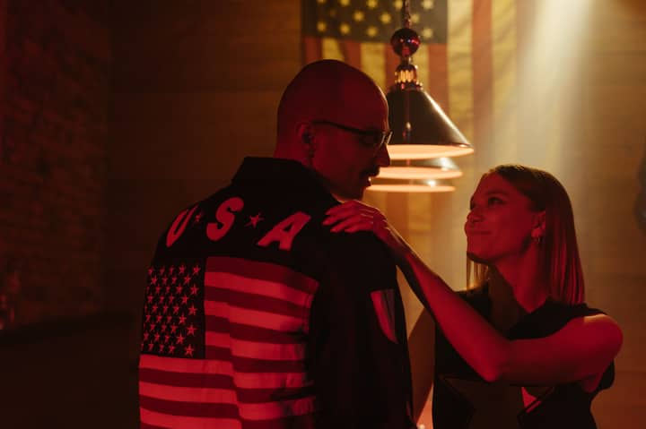 A smiling couple shares a moment under neon lights, with an American flag jacket prominent.