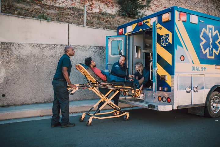 Emergency medical team helping a patient into an ambulance on a city street.