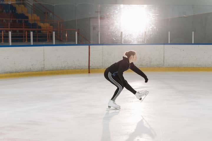 Young figure skater skillfully executes a sit spin on an indoor ice rink.