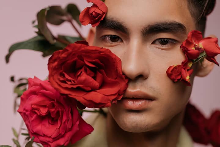 Close-up portrait of a man with red roses against a pink background, exuding elegance.