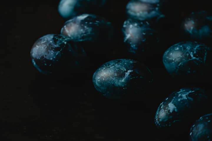 Artistic close-up of blue painted eggs on a dark surface, evoking a mysterious and elegant feel.