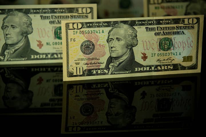Detailed image of US ten dollar bills displayed with dramatic reflection, highlighting currency design.