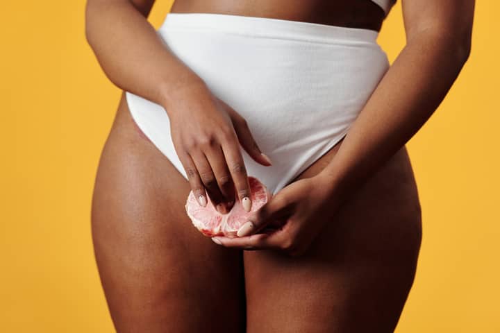 A woman in white underwear holds a pomelo slice against a vibrant yellow backdrop, showcasing fruit and fashion.