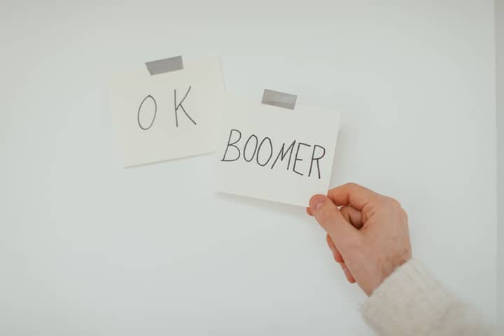 A hand holding a sticky note with the popular phrase 'OK Boomer', illustrating generational dialogue.