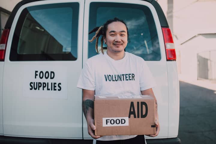 A volunteer holding a box of food aid in front of a supply vehicle, symbolizing generosity and help.