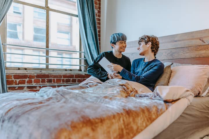 Two smiling adults in a cozy bedroom setting, sharing an intimate and joyful moment.