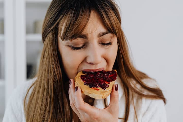 Close-up of a woman savoring a delicious peanut butter and jelly sandwich indoors.