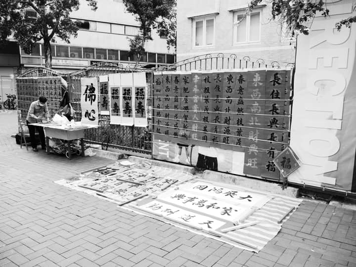 Grayscale photo of a street calligraphy stall in Hong Kong, showcasing Chinese characters.