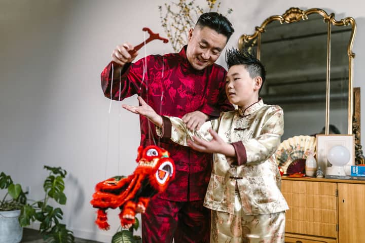 Father and son joyfully interact with a Chinese lion puppet, celebrating culture.