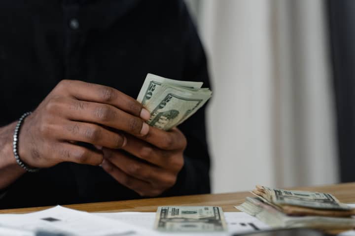 Adult counting dollar bills at a desk, focused on money management and finance.