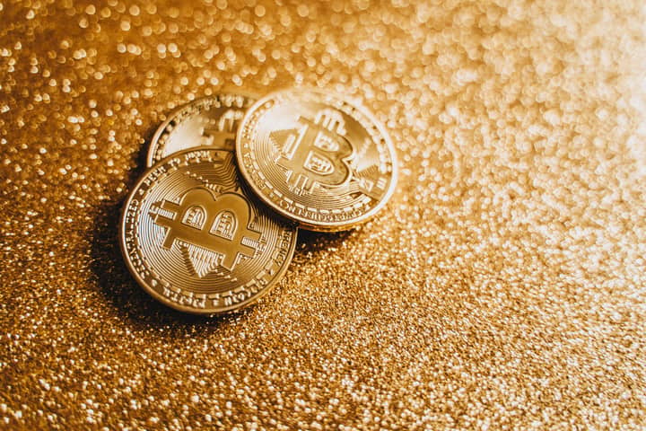 Closeup of three Bitcoin coins on a shimmering gold glitter background, symbolizing digital wealth.