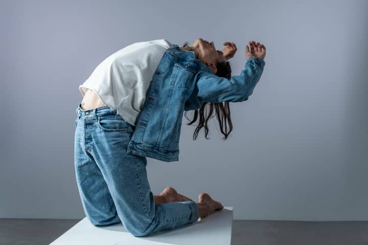 Artistic pose in denim attire captured in a minimalist studio setting.