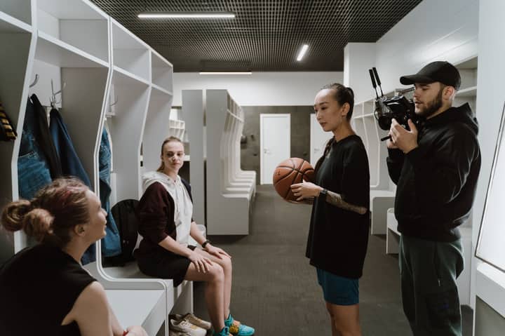 A candid behind-the-scenes look inside a basketball locker room during an interview with athletes and a cameraman.