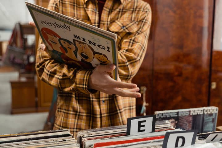 Person holding a vintage vinyl record in a music store, wearing a plaid shirt.