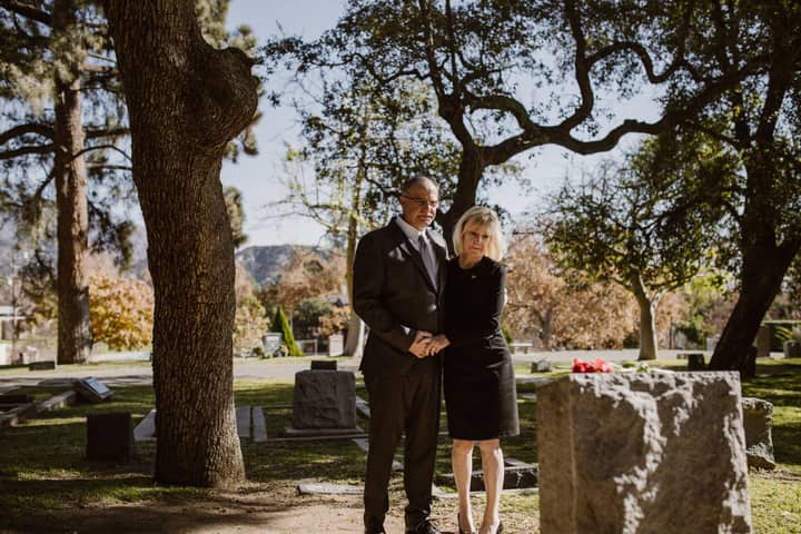 A couple stands solemnly in a serene cemetery, reflecting on memories and loss.