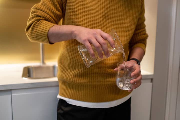 Close-up of individual pouring water into glass in a modern kitchen.