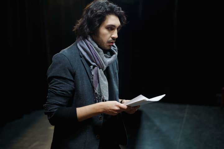 Male actor rehearsing lines on stage in a dimly lit theater environment.