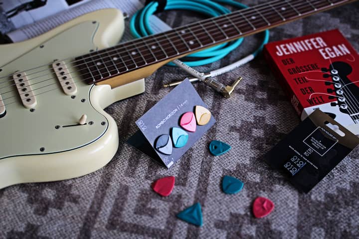 Electric guitar with colorful picks and a book on a textured surface, artistic setup.
