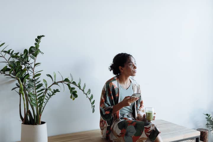 A young woman enjoys a healthy lifestyle, sipping matcha while using her cellphone indoors.