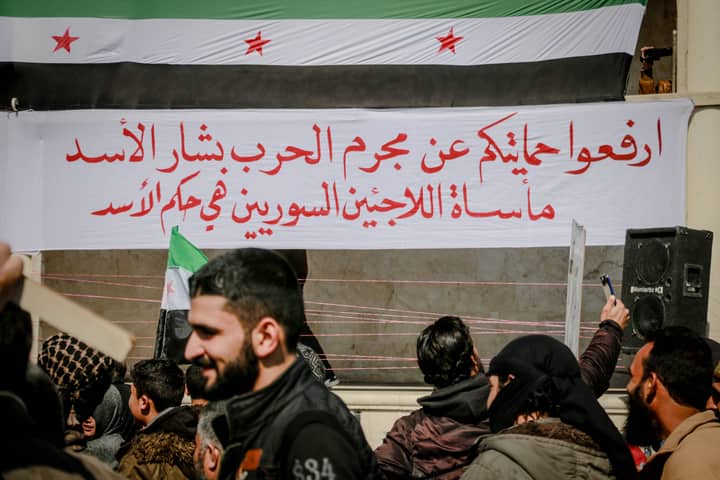 Crop anonymous ethnic male activists against Syrian flag and placard with inscription during demonstration on street