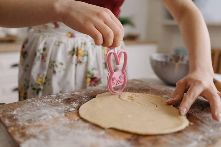 Hands cutting dough with a bunny cookie cutter on a flour-dusted surface.