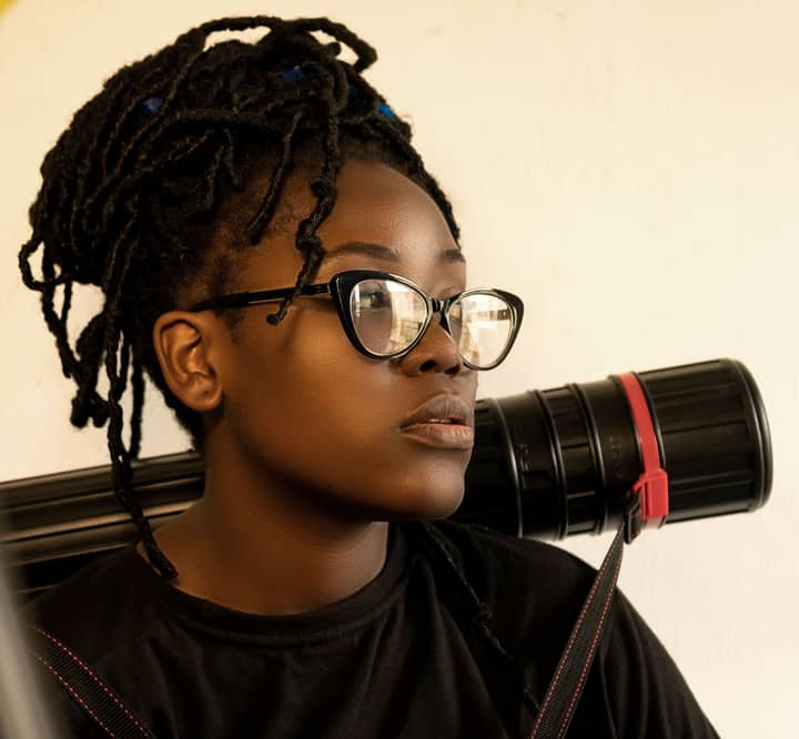 Portrait of a young woman with braided hair and glasses carrying a tube.