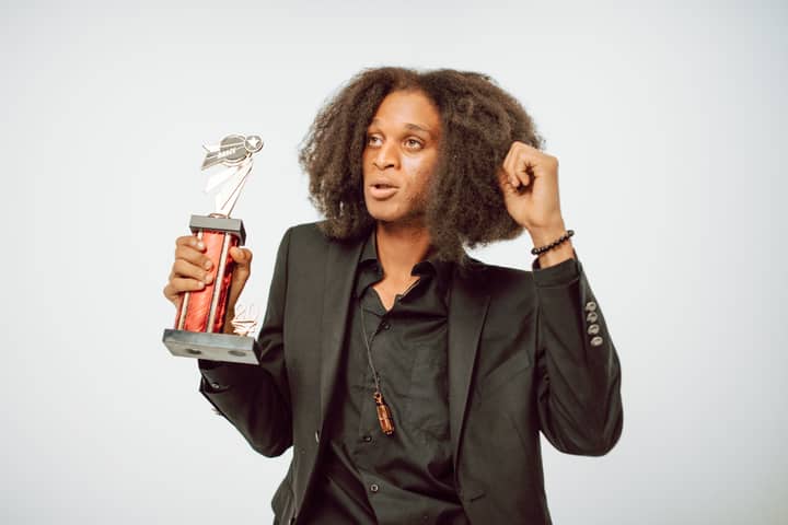 A young man with afro hair celebrates while holding a shiny award trophy.