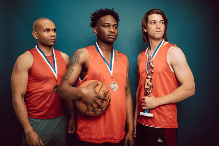 Three basketball players celebrating with medals and a trophy in victory pose.