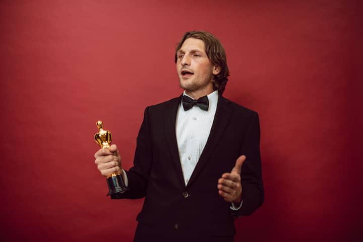 An accomplished man in a tuxedo holding a trophy, symbolizing triumph and recognition, against a red backdrop.