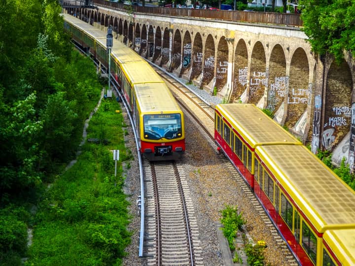 Colorful Berlin S-Bahn trains traveling on tracks beside graffiti-covered walls, capturing urban transit.