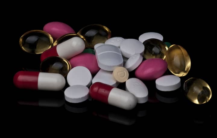 Close-up of various colorful pills and capsules on a black background.